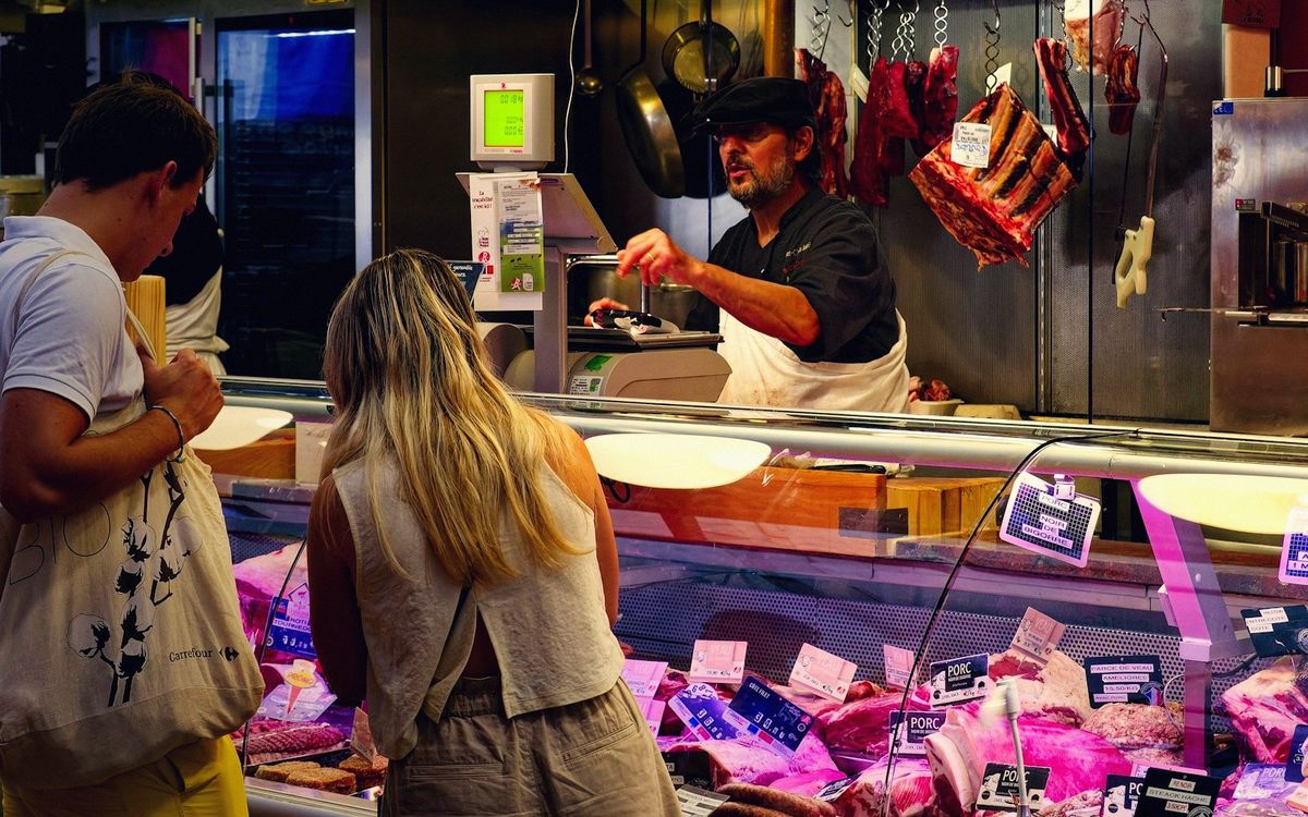 A butcher serving customers at his counter inside Talensac market